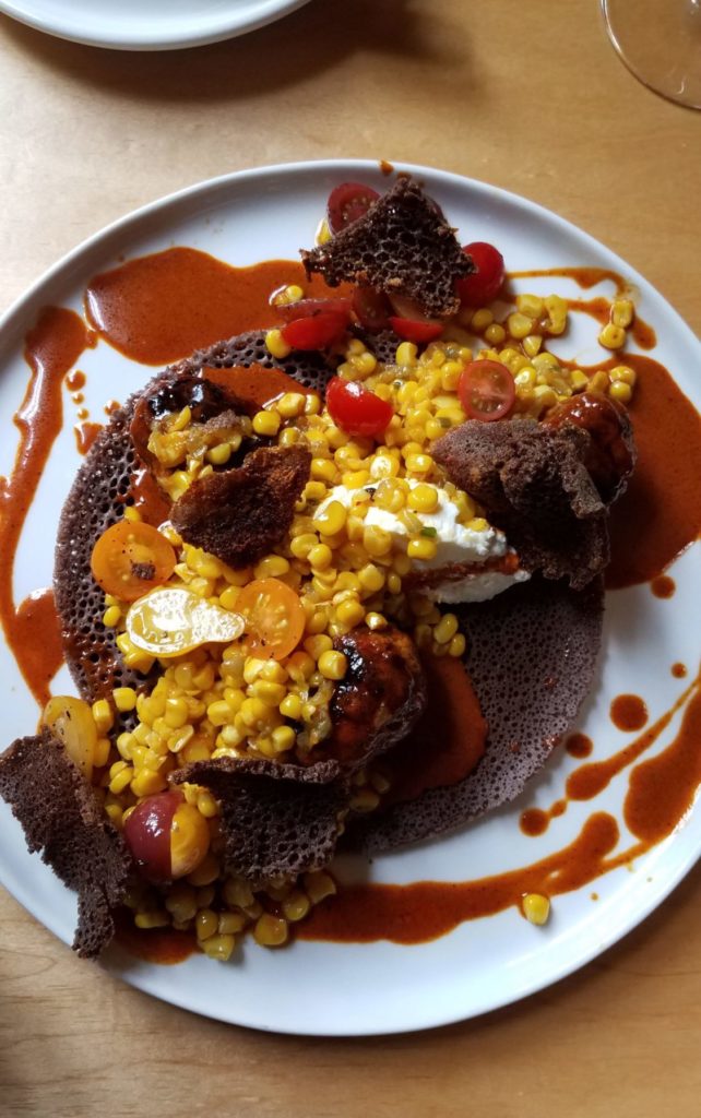 Fresh lamb sausage on Tana Market injera topped with sauteéd corn and cherry tomato, finished with whipped feta and berbere spice